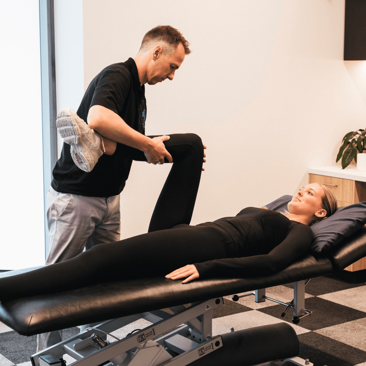 Performe physiotherapist assessing a footballer's leg on the treatment table